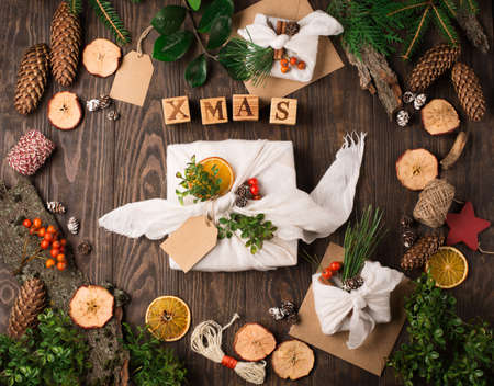 Stylish rustic gifts wrapped in linen fabric with green branches on wooden table with pine cones, oranges and apples. Flat lay. Simple eco presents plastic free. Zero waste Christmas.の写真素材