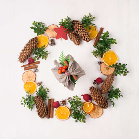 Stylish rustic gifts wrapped in linen fabric with green branches on wooden table with pine cones,...