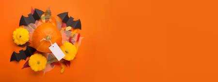 Halloween paper decorations on orange background. Black bats, pumpkins, sweets and autumn leaves. Halloween concept. Flat lay, top view, overhead. Halloween party greeting card mockup with copy space.の写真素材