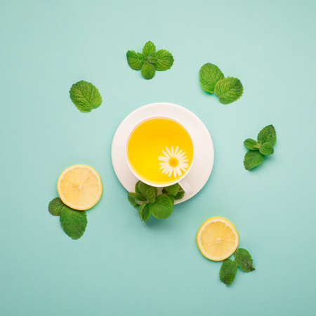 Herbal tea of chamomile flower with mint, ginger, lemon, honey on paper blue background. Spicy medicinal tea for autumn or winter season. Flat lay, top view. Healthy food and drink concept.の写真素材