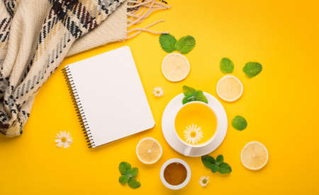 Herbal tea of chamomile flower with mint, ginger, lemon, honey on paper yellow background. Spicy medicinal tea for autumn or winter season. Flat lay, top view. Healthy food and drink concept.の写真素材