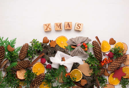 Stylish rustic gifts wrapped in linen fabric with green branches on wooden table with pine cones,...
