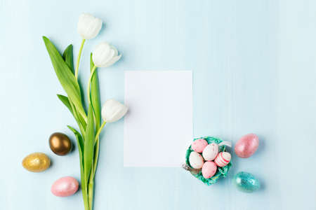 Easter greeting card with easter eggs and tulip flowers on blue wooden background. Gold, silver...