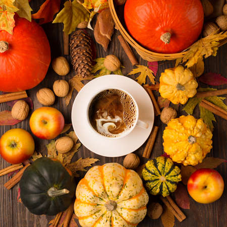 Concept of fall harvest or Thanksgiving day. Autumn composition with cup of coffee, pumpkins, apples, nuts and cinnamons on dark rustic wooden background. Top view, copy space.の写真素材