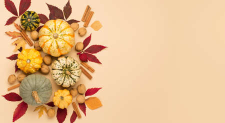 Autumn holiday composition with pumpkins, nuts and dry leaves on paper beige color background....