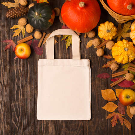 Zero waste Thanksgiving concept. Reusable shopping bag with pumpkins, apples, nuts and autumn leaves on rustic wooden background. Eco friendly autumn holidays, fall harvest. Tote bag mockup. Top view.の写真素材