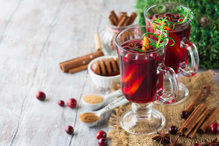 Christmas Hot mulled wine in glasses with orange slices, cranberry and cinnamon sticks on white wooden background, selective focus. Winter Holiday time concept, copy space.の写真素材