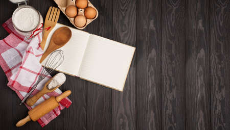 Recipe Cooking book, fresh Eggs, rolling pin, Flour and Wooden kitchen Utensils on dark rustic wooden background. Top view, copy space. Preparation cooking concept.の写真素材