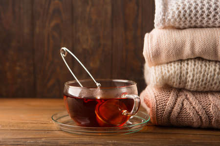 Stack of cozy knitted sweaters and cup of hot tea on rustic wooden background. Copy space, selective focus. Winter Christmas time conceptの写真素材