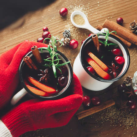 Christmas Hot mulled wine with orange slices, cranberry and cinnamon sticks in female hands on...