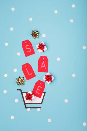 Super Sale day or Singles day concept. Shopping trolley, gift boxes and red tags on blue paper background. Online shopping of China. Top view, flat lay, copy space.