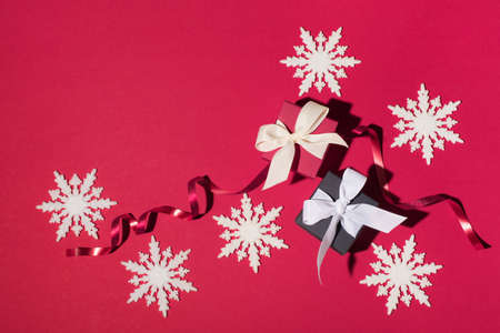 Top view of black and red Christmas boxes with red ribbon and white snowflakes on red background....