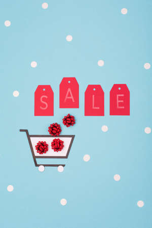 Super Sale day or Singles day concept. Shopping trolley, gift boxes and red tags on blue paper...