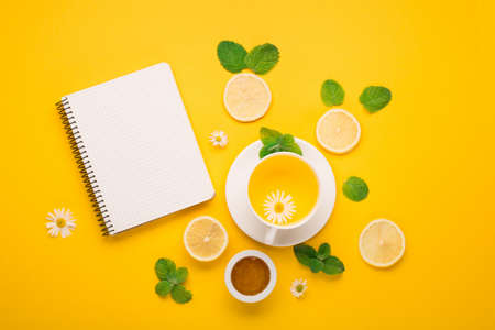 Herbal tea of chamomile flower with mint, ginger, lemon, honey on paper yellow background. Spicy medicinal tea for autumn or winter season. Flat lay, top view. Healthy food and drink concept.の写真素材