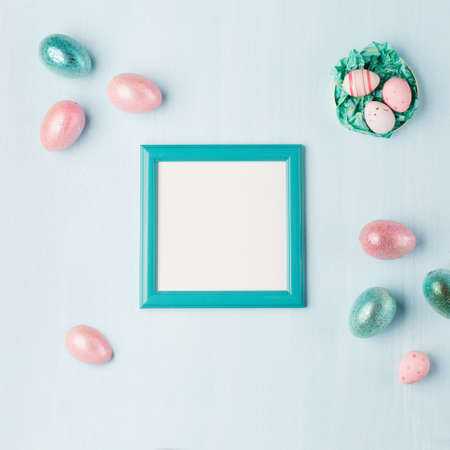 Pastel shiny Easter eggs on blue wooden background, dark blue frame with space for text. Flat lay, top view, copy space. Easter decoration, foil minimalist egg design, modern festive card template.の写真素材