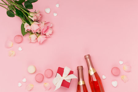 Festive holiday greeting card for Valentines, Birthday, Woman or Mothers Day. Flowers, bottle of wine, sweets and gift on pink background. Valentines day concept. Flat lay, top view, copy space.の写真素材