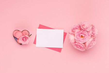 Festive holiday greeting card for Valentines, Birthday, Woman or Mothers Day. Flowers roses, envelope and sweets macaroons on pink background. Valentines day concept. Flat lay, top view, copy space.の写真素材