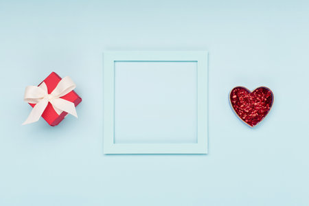 Valentines Day concept. Blue empty frame, gift and red glitter heart on pastel blue background. Flat lay, top view, copy space. 8 March, Valentines Womens Mothers Day, Birthday holiday festive card.の写真素材