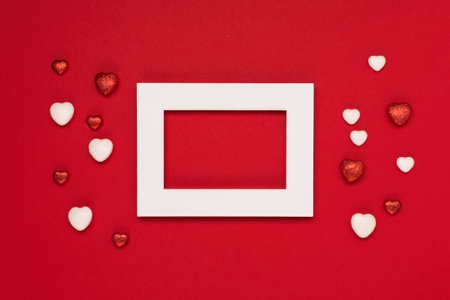 Red white hearts and empty frame on red background. Valentines day concept. Festive holiday greeting card for Valentines, Birthday, Woman, Mothers Day. Flat lay, top view, copy space.の写真素材