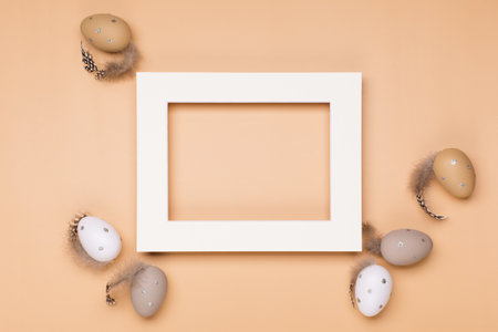 Craft Easter eggs and empty frame on beige pastel background, space for text. Flat lay, top view....