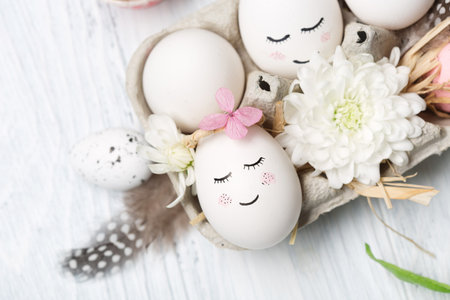 Holiday creative Easter concept with white cute eggs, tree branches, quail feathers and spring flowers on white wooden background. top view, copy space. Easter festive greeting card.の写真素材