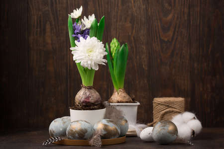 Festive Easter holiday greeting card background. Easter Decoration with gray golden eggs, quail feathers, hyacinth daisy flowers on dark wooden background. Happy Easter card concept.の写真素材