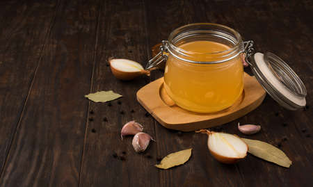 Traditional homemade beef bone broth with vegetable in glass jar on dark rustic wooden background. Healthy low-calories collagen food concept. Selective focus, copy space.の写真素材