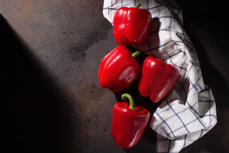 Food cooking background. Fresh sweet red peppers and textile white blue towel on dark rustic wooden background. Top view, copy space. Fresh healthy food, vegan diet concept.の写真素材