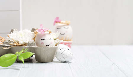 Holiday creative Easter concept with white cute eggs, tree branches, quail feathers and spring flowers on white wooden background. Selective focus, copy space. Easter festive greeting card.の写真素材