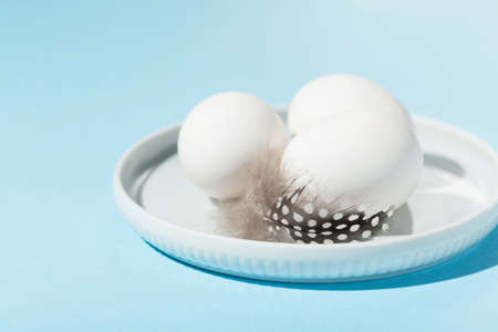 Festive Easter holiday greeting card background. Easter white eggs and feathers on blue table. Copy...