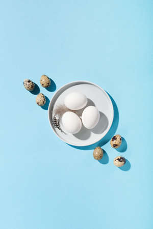Festive Easter holiday greeting card background. Easter white eggs and feathers on blue table. Copy...