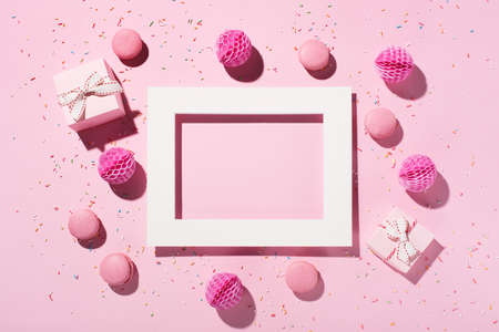 Happy birthday or party background. White empty frame, sweet cakes macaroons, sprinkles, pink gift...