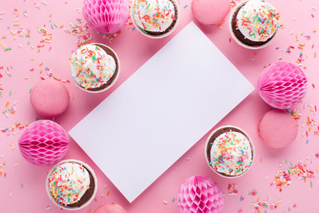 Festive holiday greeting card for Birthday, Woman or Mothers Day. Empty white blank, gift box, paper decorations and cupcakes on pink sprinkles background. Flat lay, top view, copy space.の写真素材