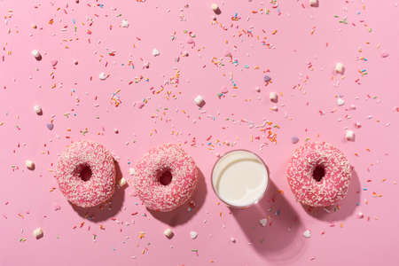 Happy National donut day concept. Donuts with pink icing, glass of milk and sugar sprinkle on pink background. Top view, copy space.の写真素材