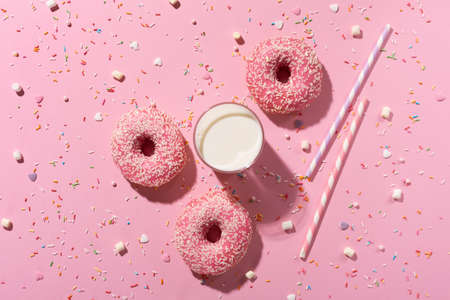 Happy National donut day concept. Donuts with pink icing, glass of milk and sugar sprinkle on pink background. Top view, copy space.の写真素材