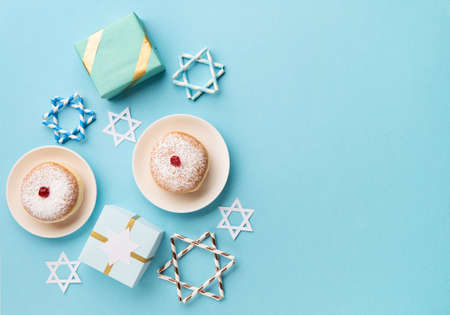 Hanukkah sweet donuts sufganiyot with powdered sugar and fruit jelly jam, gift boxes on blue paper...