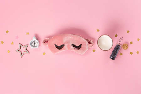 Sleeping mask, candle, lavender and alarm clock on pink pastel background. Quality of sleep, good night, insomnia, relaxation concept. Flat lay, top viewの写真素材