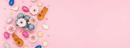 Happy Easter holiday greeting card. Homemade Easter bunny buns, sugar cookies, chocolate eggs, flowers on paper pink background. Festive Easter breakfast concept. Copy space, top view.の写真素材
