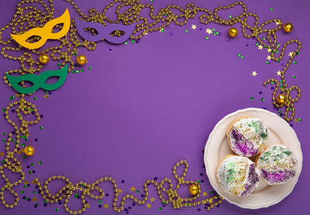 Mardi Gras King Cake sufganiyot donuts, masquerade festival carnival masks, gold beads and golden, green, purple confetti on purple background. Holiday party invitation, greeting card concept.の写真素材