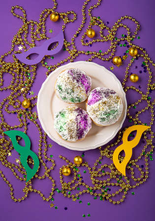 Mardi Gras King Cake sufganiyot donuts, masquerade festival carnival masks, gold beads and golden, green, purple confetti on purple background. Holiday party invitation, greeting card concept.の写真素材