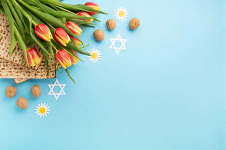 Jewish holiday Passover greeting card concept with matzah, nuts, daisy and tulip flowers on blue...
