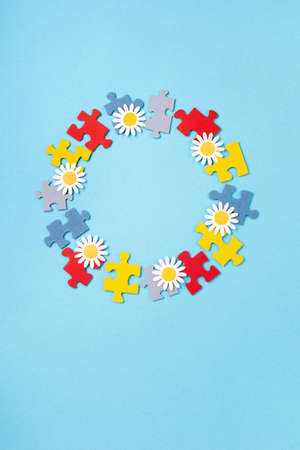World Autism Awareness Day or month concept. Creative design for April 2. Color puzzle, symbol of awareness for autism spectrum disorder and daisy flowers on blue background. Top view, copy space.の写真素材
