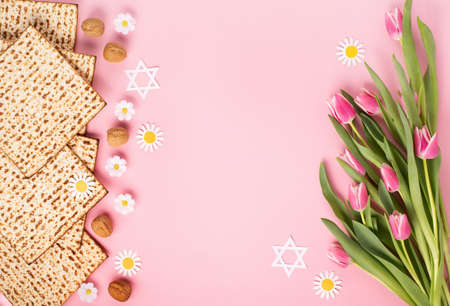 Jewish holiday Passover greeting card concept with matzah, nuts, tulip and daisy flowers on pink...