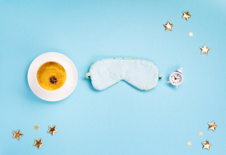 World Sleep day observed on March. Quality of sleep, good night, insomnia, relaxation concept. Sleeping mask, Turmeric golden milk latte and white alarm clock on blue background. Flat lay, top viewの写真素材