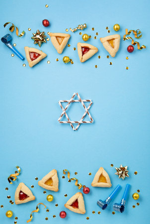 Purim celebration jewish carnival holiday concept. Tasty hamantaschen cookies, Carnival noisemakers, sweet candies and party decor on blue background. Top view, flat lay, copy space.の写真素材