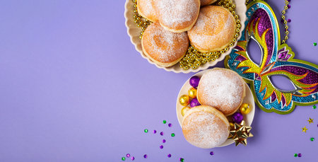 Mardi Gras King Cake donuts or donuts, masquerade festival carnival mask, gold beads and golden, green confetti on purple background. Holiday party invitation, greeting card concept.の写真素材