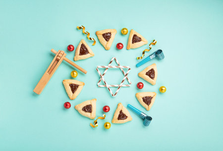 Purim celebration jewish holiday concept. Tasty hamantaschen cookies, Triangular pastry, Carnival mask, noisemaker, sweet candies and festive party decor on mint green background, Top view, copy spaceの写真素材