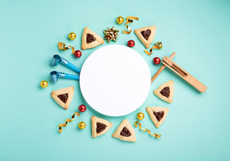 Purim celebration jewish holiday concept. Tasty hamantaschen cookies, Triangular pastry, Carnival mask, noisemaker, sweet candies and festive party decor on mint green background, Top view, copy spaceの写真素材