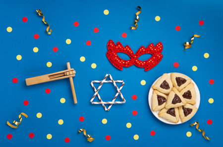 Homemade Purim hamantaschen cookies, Triangular pastry, Carnival mask, noisemaker, sweet candies and festive party decor on dark blue background, Top view. Purim celebration jewish holiday concept.の写真素材