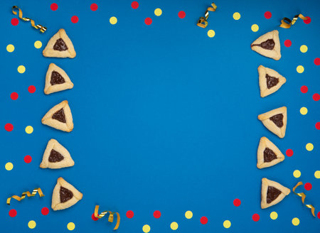 Homemade Purim hamantaschen cookies, Triangular pastry, Carnival mask, noisemaker, sweet candies and festive party decor on dark blue background, Top view. Purim celebration jewish holiday concept.の写真素材